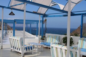 A covered outdoor seating area with white and blue furniture, overlooking a coastal landscape.