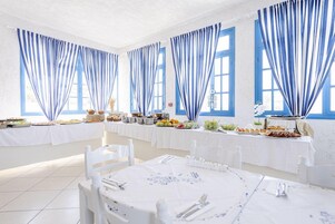 A dining area with white tables and chairs, blue curtains, and a buffet with various food items.