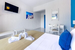 Habitación de hotel con cama, escritorio, silla, televisión montada en la pared y un cuadro de una escena costera.