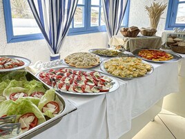 Una mesa de buffet con diversos platos griegos, un cartel que dice 'Greece' y vistas al exterior a través de una ventana.