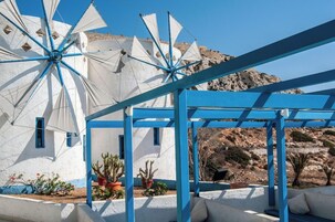 Un edificio blanco con detalles azules, un molino y una pérgola azul con plantas en macetas.