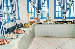 Una mesa de buffet con diversos platos, una silla y una ventana con cortinas azules.