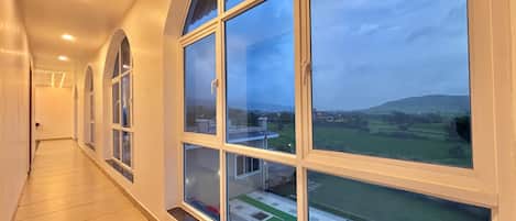 Un pasillo con amplios ventanales que ofrecen vistas a un paisaje verde y colinas distantes.