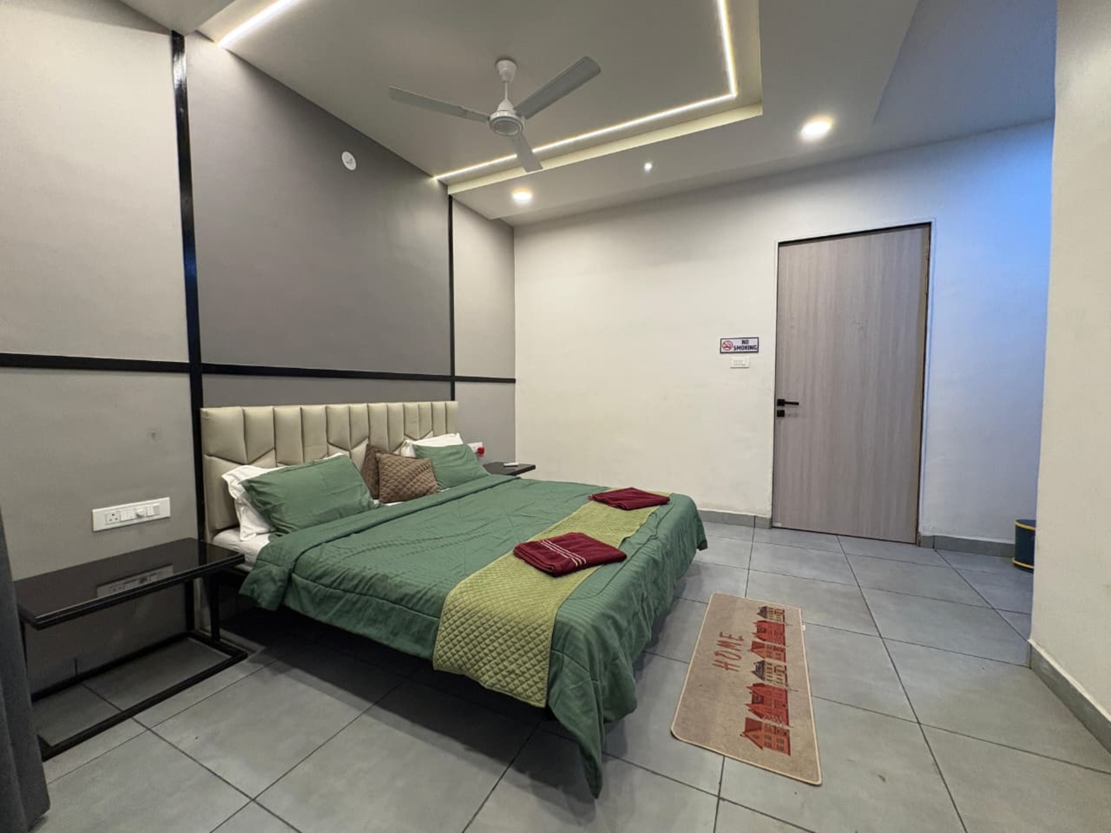 Una habitación de hotel con una cama, un ventilador de techo, una puerta y un cartel de no fumar.