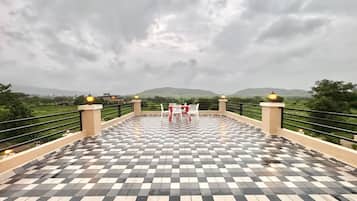 A checkered outdoor terrace with a table and chairs, surrounded by a railing and overlooking a hilly landscape.