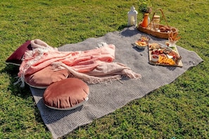 A picnic setup on a grassy field with a blanket, pillows, a basket with food, and a lantern. - Charming Tiny Home for a Nature Escape in the Golden Plains Shire near Ballarat, Victoria (Ross Creek)