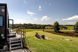 A wooden deck with outdoor seating, a fire pit, and a view of a green landscape. - Charming Tiny Home for a Nature Escape in the Golden Plains Shire near Ballarat, Victoria (Ross Creek)