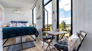 A bedroom with a bed, a small table, and a chair, a balcony with a view, and a window.