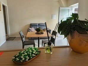 A dining area with a table, chairs, a potted plant, a tray of candies, and a bottle of perfume.