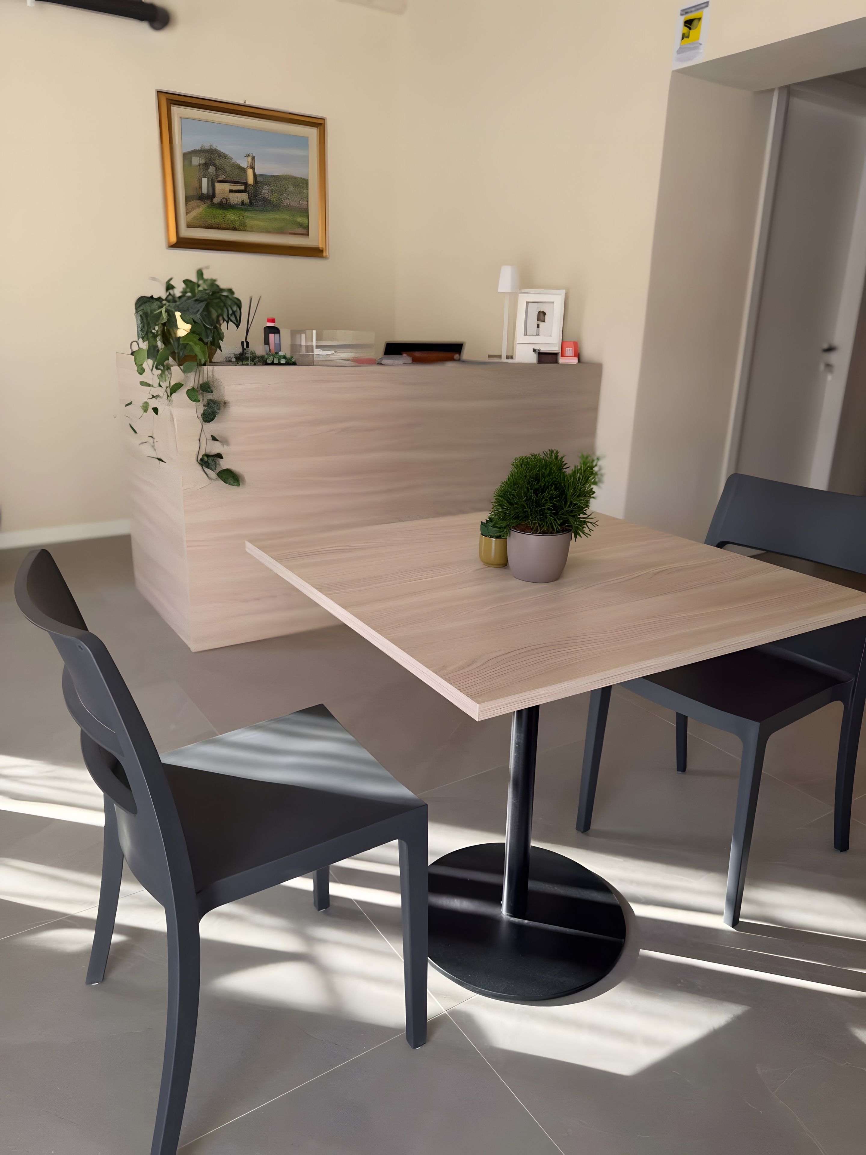 Un espace repas moderne avec une table en bois, deux chaises, une plante en pot et un tableau encadré au mur.