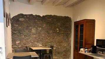 Una cucina compatta con parete in pietra, zona pranzo con sedie e un armadietto in legno.