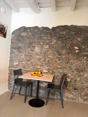 A dining area with a table and chairs, a stone wall, and a ceiling with exposed beams.