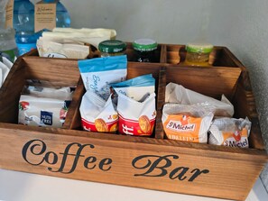 Una caja de madera con la etiqueta 'Coffee Bar' que contiene varios aperitivos y condimentos envasados.