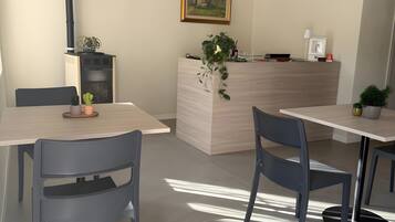 Ein moderner Essbereich mit zwei Tischen und Stühlen, einem Holzbüroempfang, einem gerahmten Bild an der Wand und einer schwarzen Rohrleitung entlang der Decke.