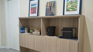 Une pièce avec une étagère en bois adossée à un mur, sur laquelle sont disposés des tableaux encadrés, une machine à café et une bouilloire.