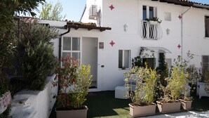Un bâtiment blanc avec un toit recouvert de tuiles, des plantes en pot et un petit espace extérieur aménagé avec des sièges.