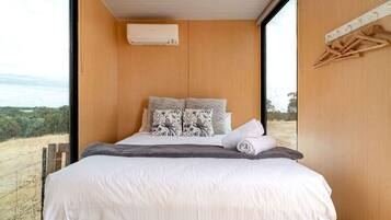 Een slaapkamer met een groot raam, een bed met wit beddengoed en een wandairconditioner.