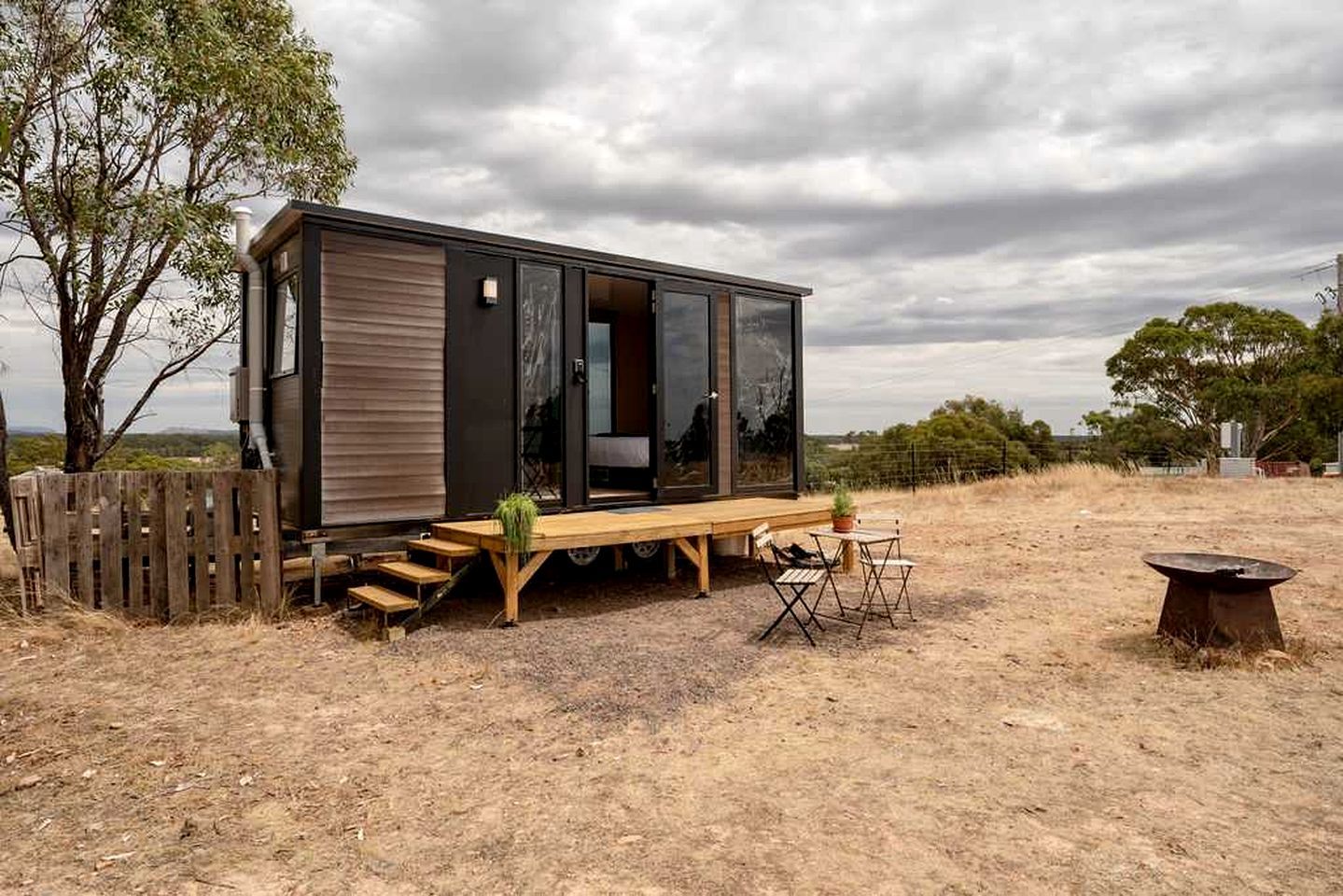 A modern cabin with a wooden deck, a dining area, and a fire pit.