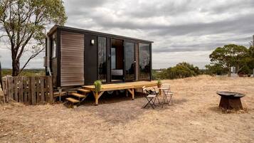 A modern cabin with a wooden deck, a dining area, and a fire pit.