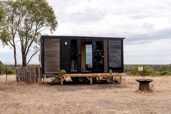 A mobile home with a sliding door, a small table, and a fire pit. - Hill View Glamping in a Victoria Tiny House (Balmattum)