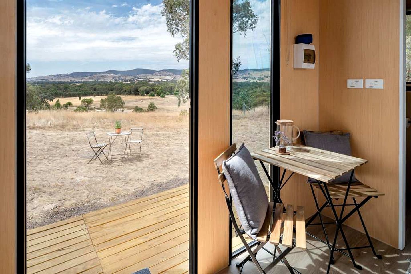 Une pièce avec vue sur un paysage aride, une table avec des chaises et une fenêtre donnant sur les collines.
