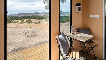 A room with a view of a dry landscape, a table with chairs, and a window with a view of the hills.
