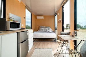 A compact bedroom with a bed, bedside table, and a view of the outdoors.