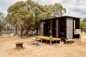 A small, single-story cabin with a wooden deck, a table, and a bench.