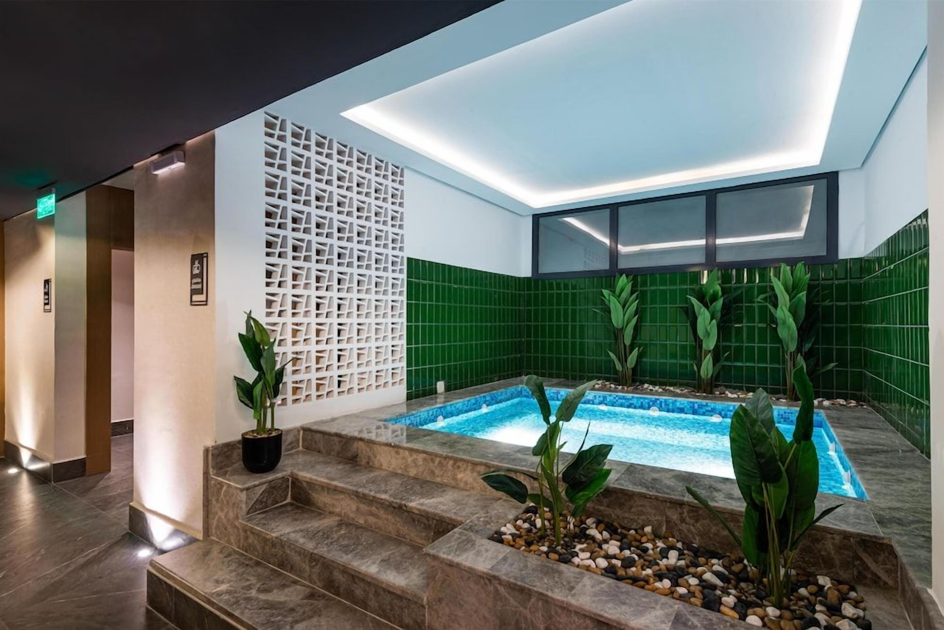 Un área de piscina interior moderna con diseño de pared geométrico, una pequeña cascada y escalones que conducen a la piscina.