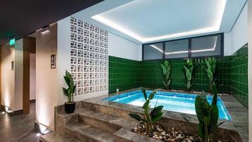 Un área de piscina interior moderna con diseño de pared geométrico, una pequeña cascada y escalones que conducen a la piscina.