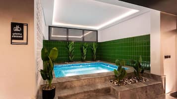 A spa area with a hot tub, green tiled walls, and potted plants.