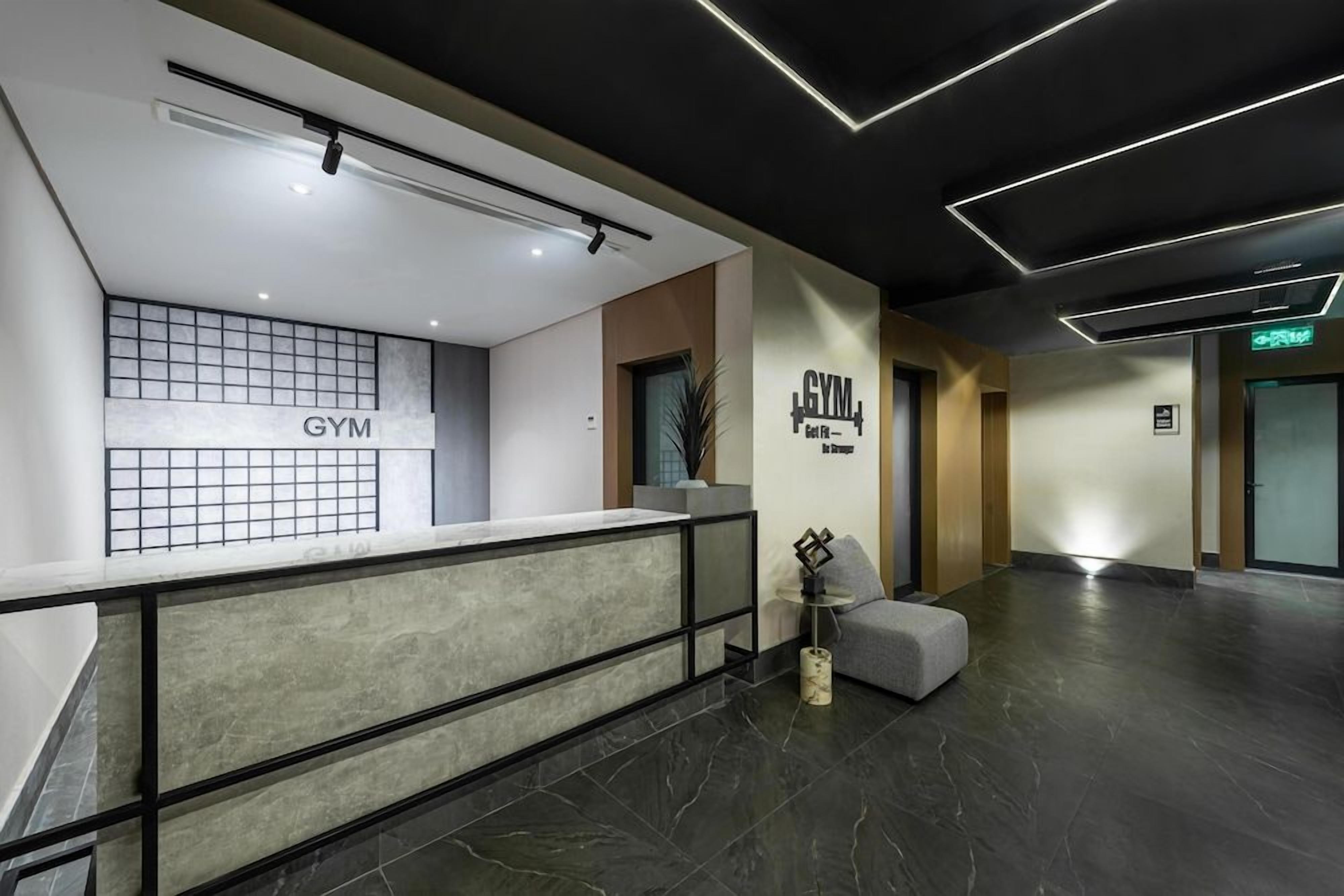 A modern gym interior with a reception desk, a wall-mounted sign, and a seating area.