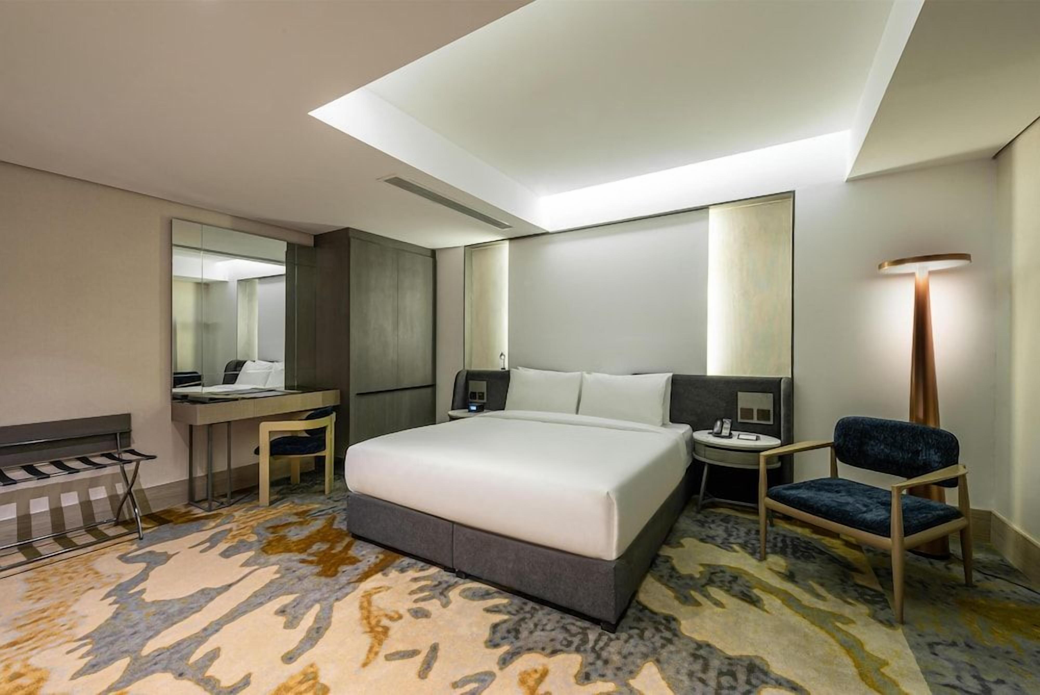 Quarto de hotel com cama, escrivaninha, cadeira e um espelho grande.