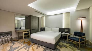 Quarto de hotel com cama, escrivaninha, cadeira e um espelho grande.