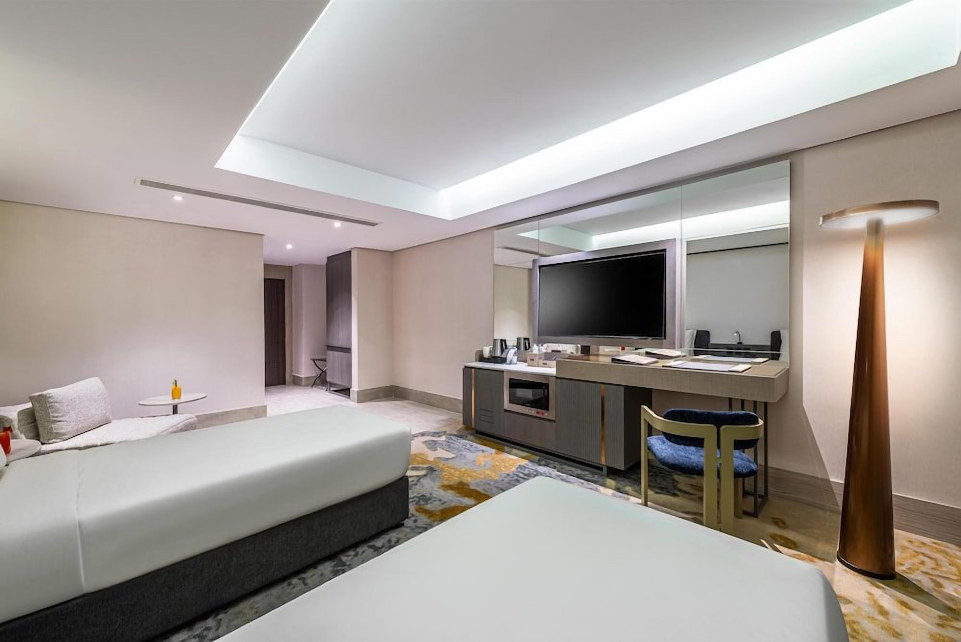 Habitación de hotel con cama, escritorio con televisor de pantalla plana, espejo y lámpara.