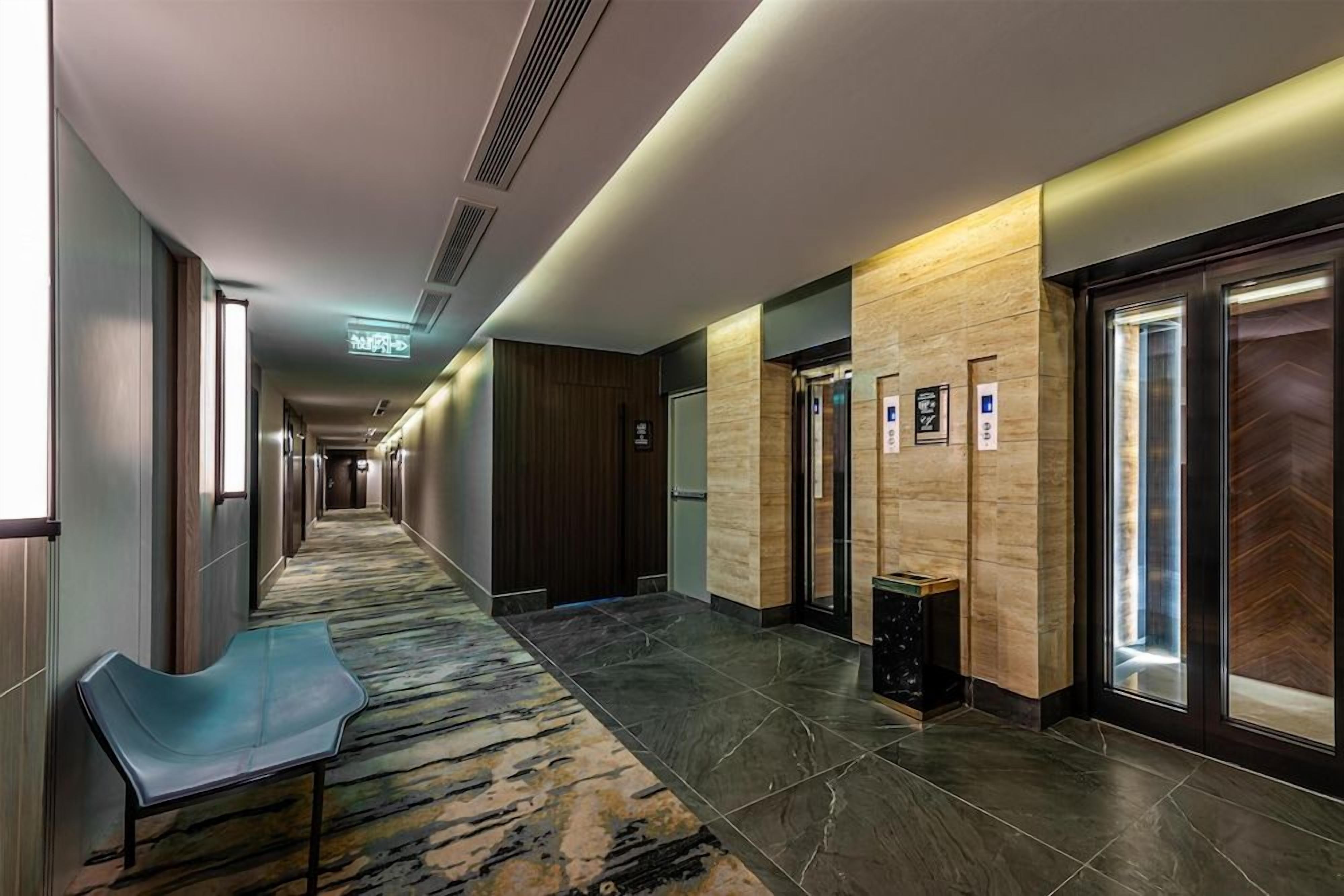 Un pasillo de hotel con piso alfombrado, un banco y un basurero.