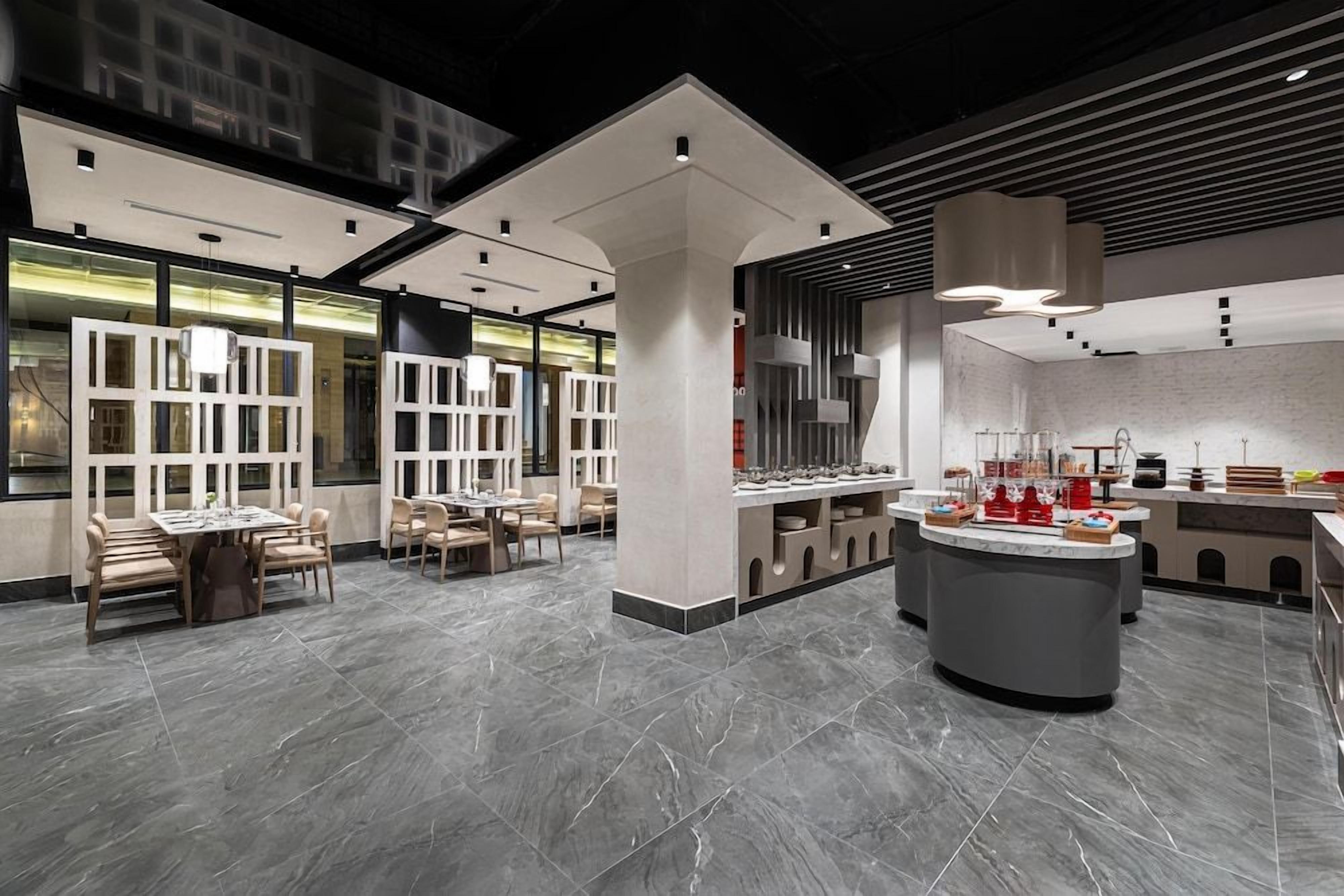 A modern interior with a central bar area, seating arrangements, and a large window providing natural light.