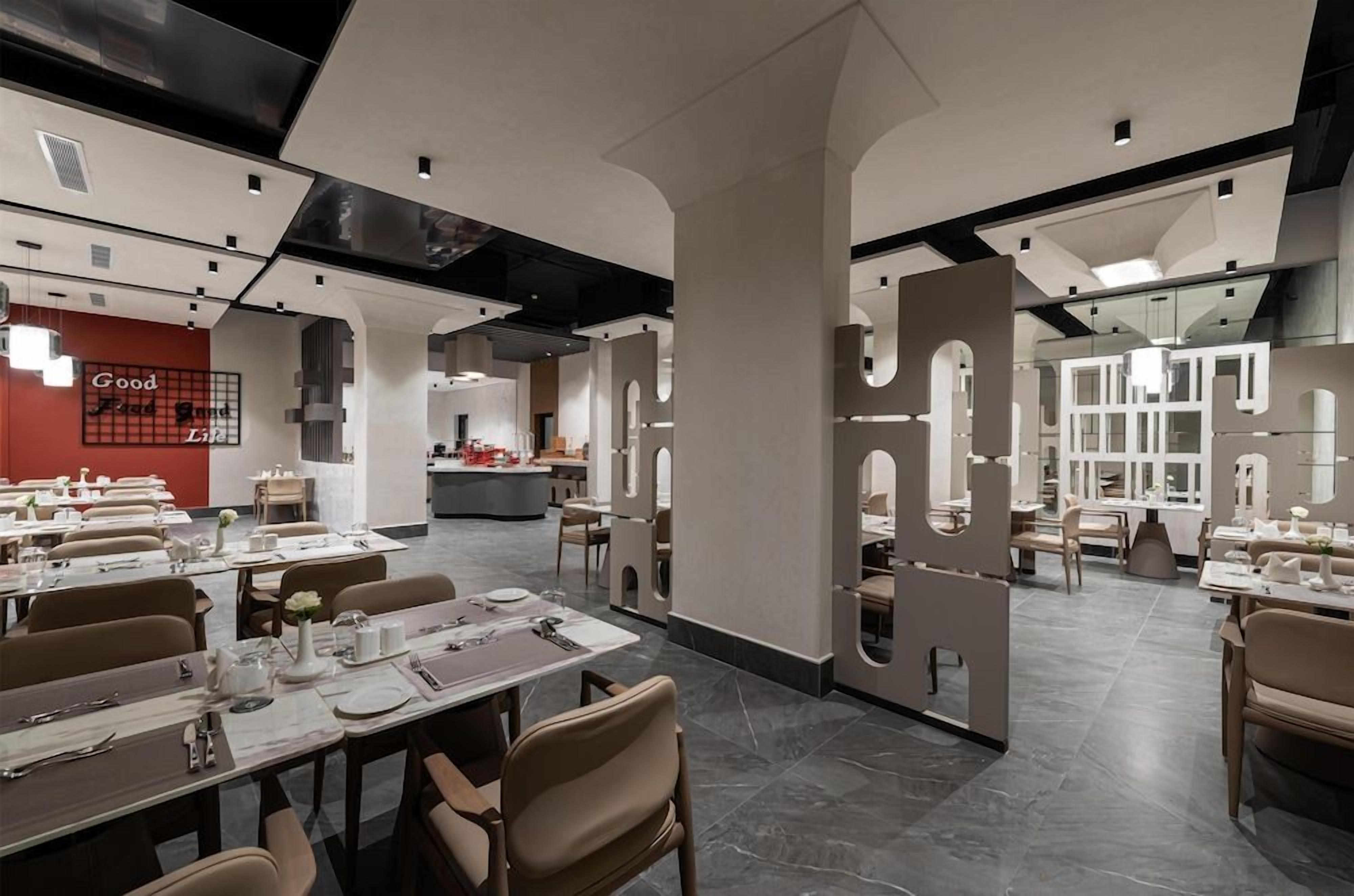 Un restaurante moderno con varias zonas de comedor, una cocina a la vista y una pared de acento roja con texto.
