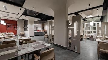 Un restaurante moderno con varias zonas de comedor, una cocina a la vista y una pared de acento roja con texto.