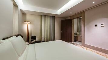 Una habitación de hotel con una cama grande, un escritorio, una silla, una lámpara y un armario.
