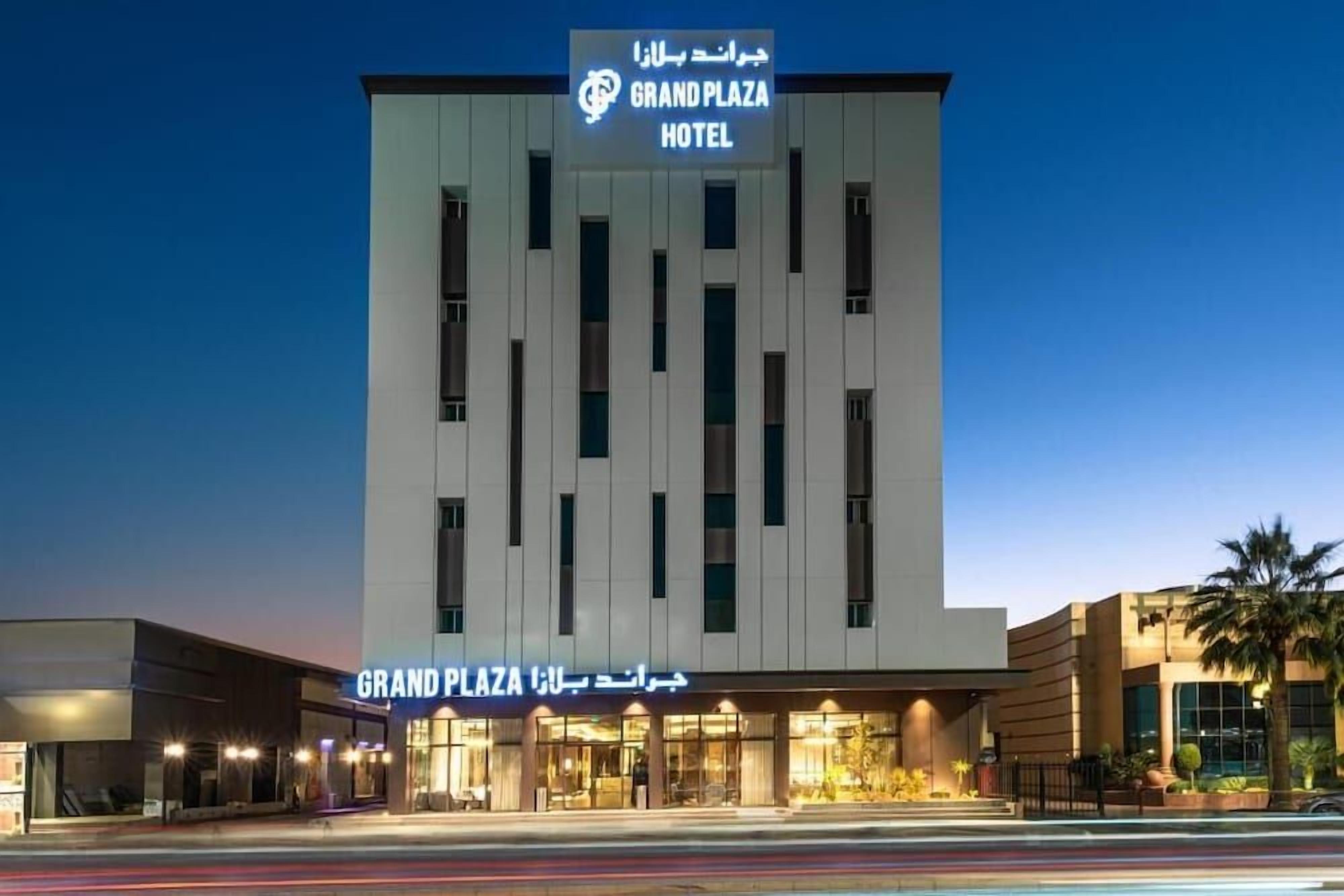 Un hotel llamado Grand Plaza, con fachada moderna, múltiples ventanales y un cartel en inglés y árabe.