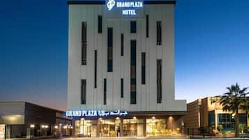 Un hotel llamado Grand Plaza, con fachada moderna, múltiples ventanales y un cartel en inglés y árabe.