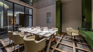 Una sala de conferencias moderna con un panel de vidrio, una mesa larga con sillas y una pared de acento verde.