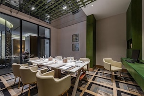 Una sala de conferencias moderna con un panel de vidrio, una mesa larga con sillas y una pared de acento verde.