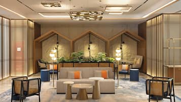 A modern lobby with a central seating area, multiple light fixtures, and a decorative plant arrangement.