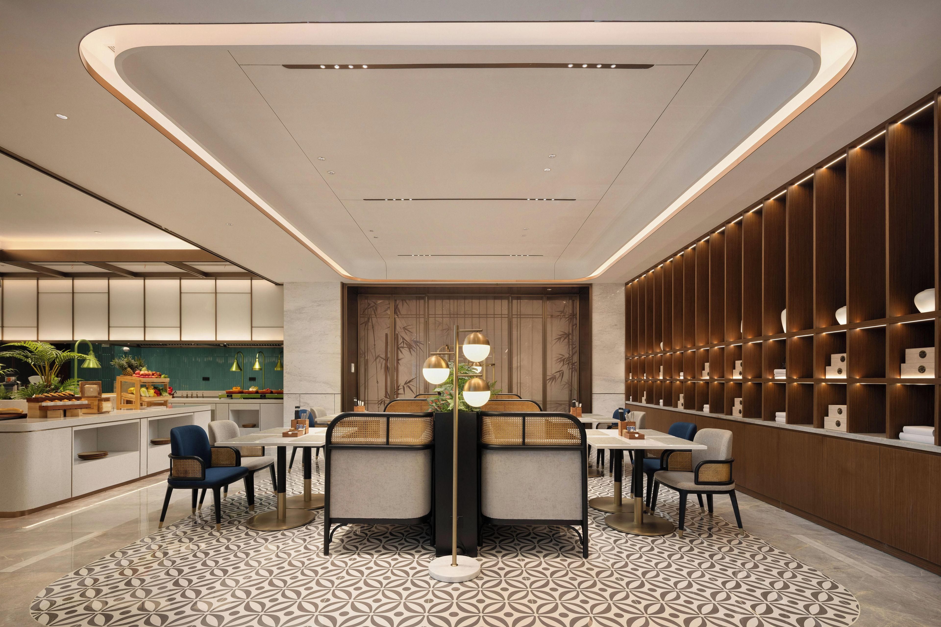Un moderno hall de hotel con un área de estar central, una cocina al fondo y una pared de madera con estanterías integradas.