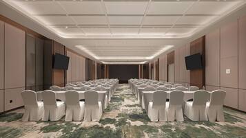 Un salón de conferencias con filas de mesas y sillas, equipado con botellas de agua y piso alfombrado.