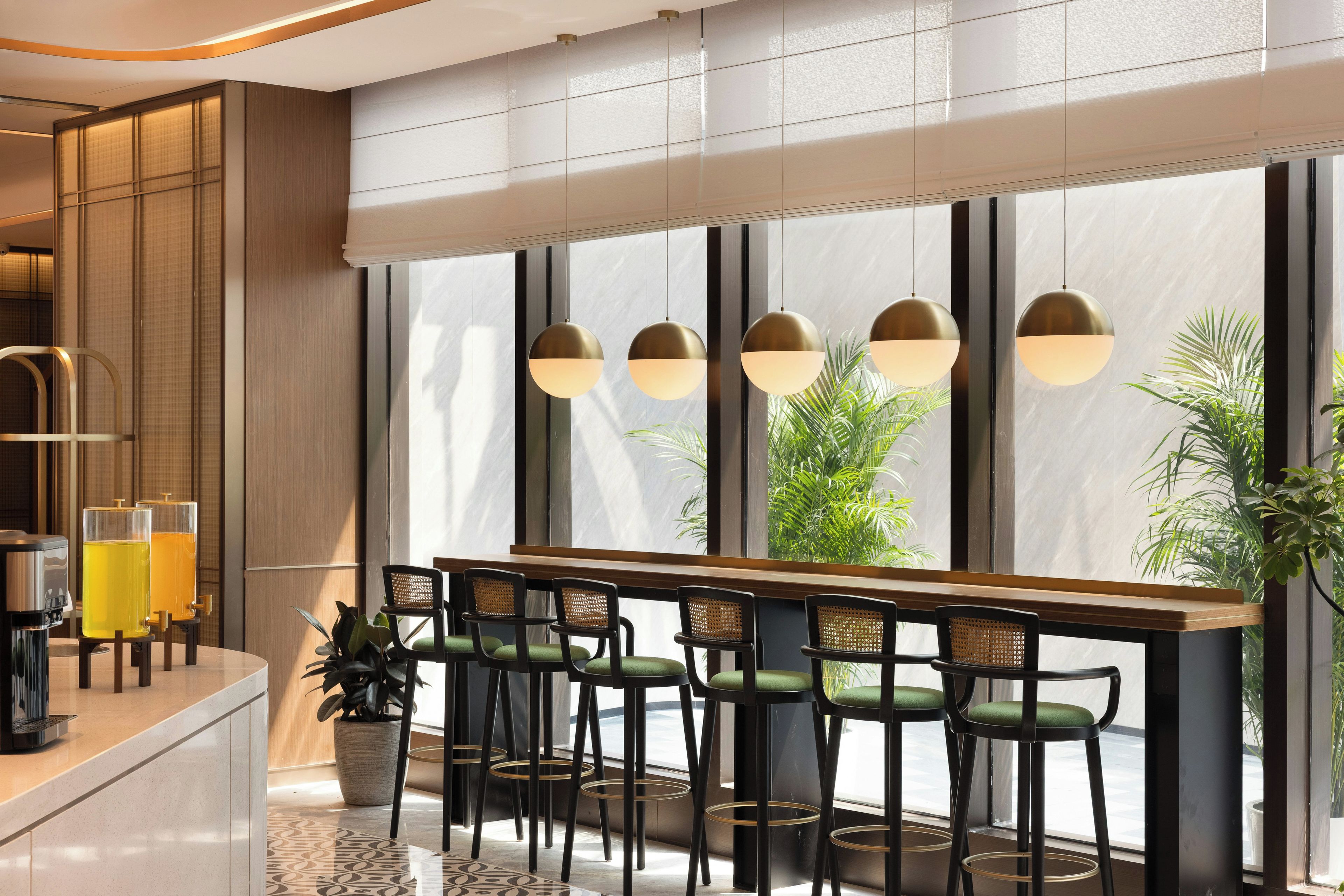 Un área de bar moderna con una barra larga, varios taburetes y un ventanal con vistas a zonas verdes.