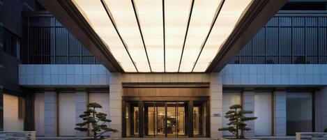A modern building entrance with a covered walkway, glass doors, and potted plants.