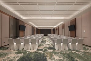 Un salón de conferencias con filas de mesas y sillas, equipado con botellas de agua y piso alfombrado.
